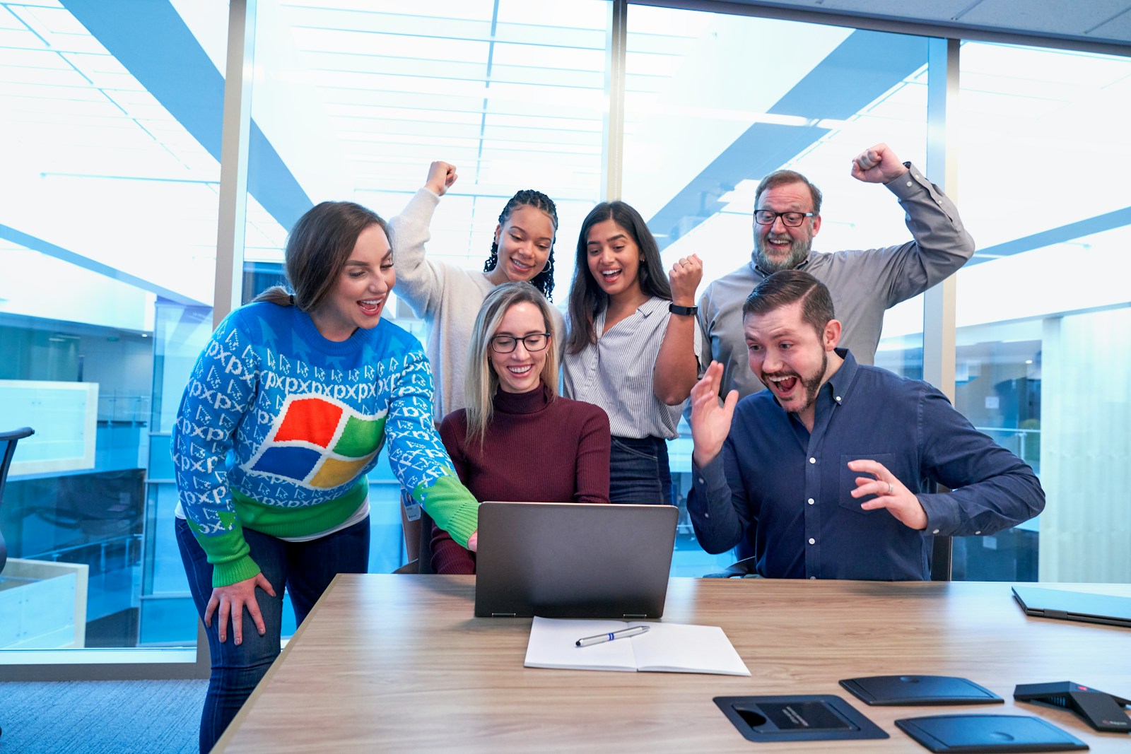 men and women sitting and standing by the table looking happy while staring at laptop